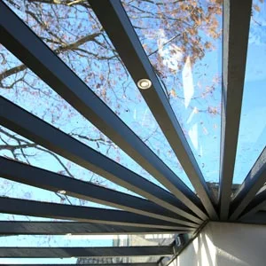 Terrassendach mit transparenten Glasplatten und integrierter LED-Beleuchtung, das einen klaren Blick auf den blauen Himmel und herbstliche Bäume bietet.