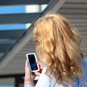 Frau mit Fernbedienung zur Steuerung einer Markise, im Hintergrund moderne Terrassenüberdachung. Komfortable Bedienung für Sonnenschutzsysteme.