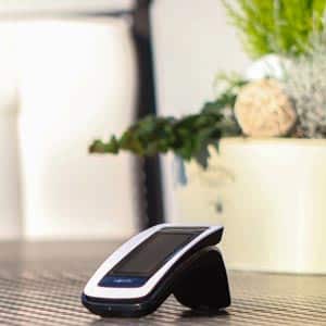 Smart-Home-Fernbedienung für Markisensteuerung, elegant präsentiert auf einem Tisch mit dekorativen Pflanzen im Hintergrund. Moderne Technologie für komfortable Bedienung.